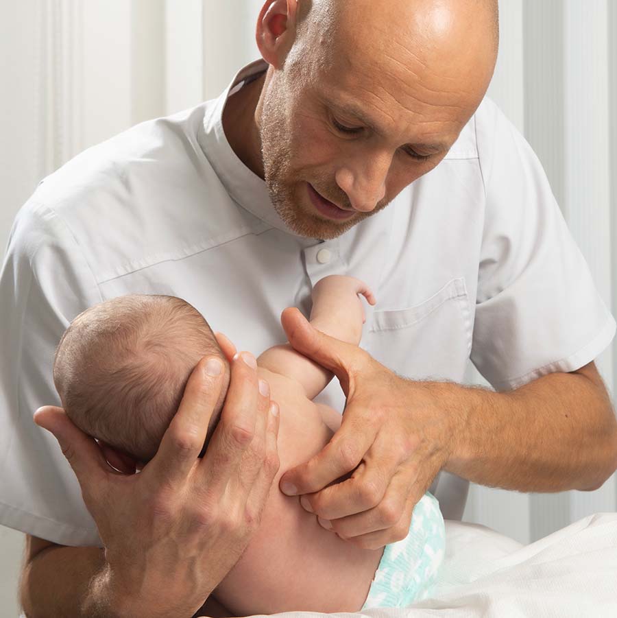 ostéopathe manipulant doucement un nourrisson en consultation à Nyon